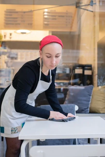 A woman carefully wraps a sofa in protective material while packing boxes in a bright room.